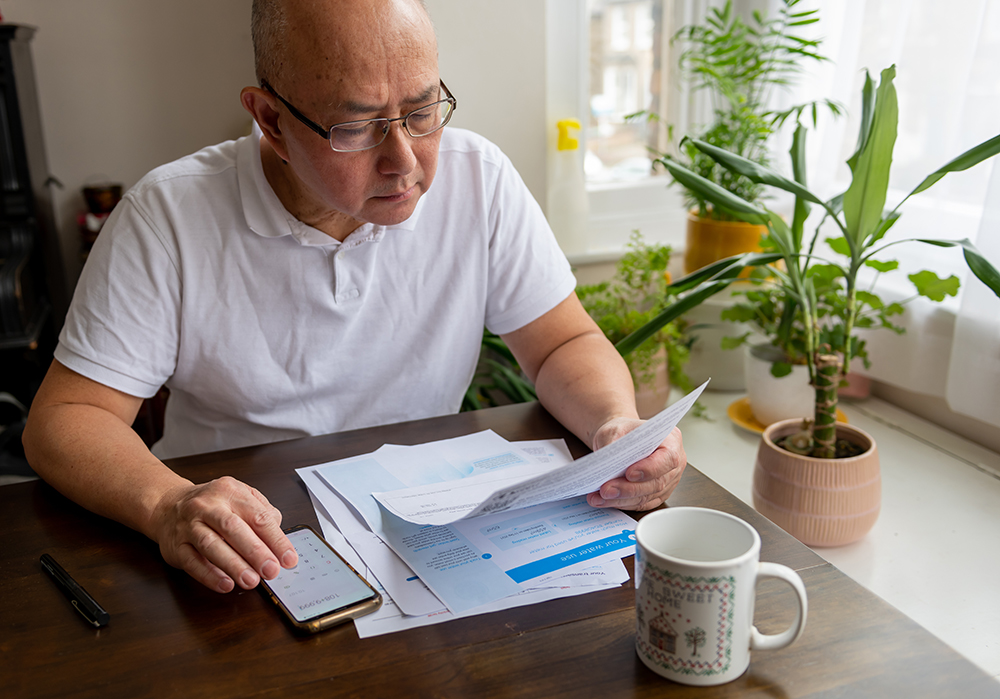 A senior man sitting by a table calculating the cost of energy bills. 