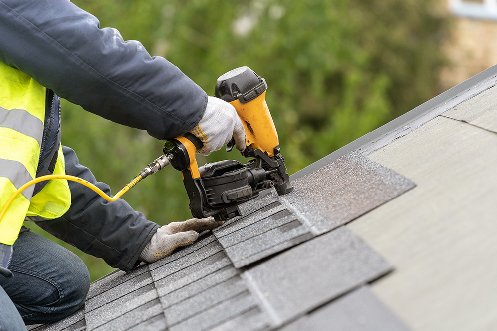 Workman installing shingles on roof of a house.