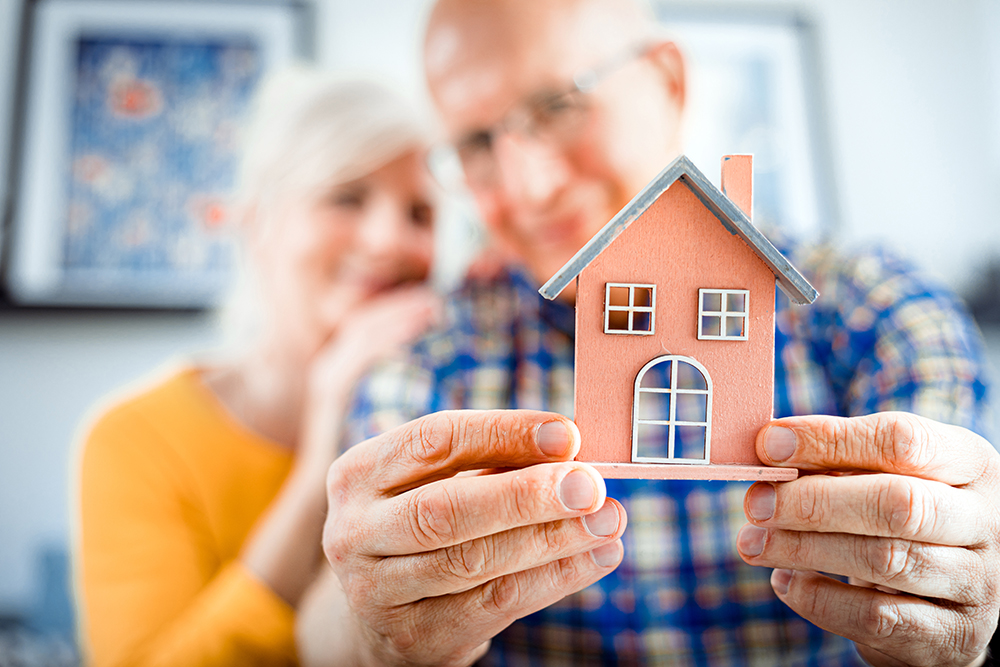 Happy senior couple holding small home model