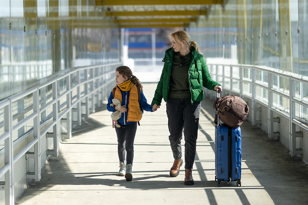 Ukrainian immigrant mother with child with luggage walking at train station.
