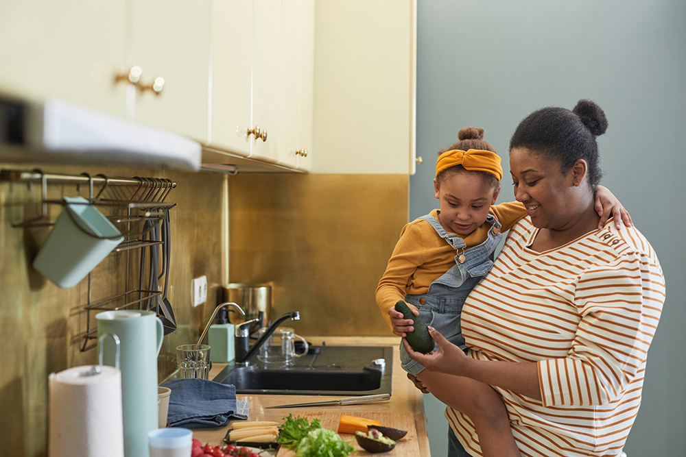 Black mother holding daughter while cooking together in kitchen