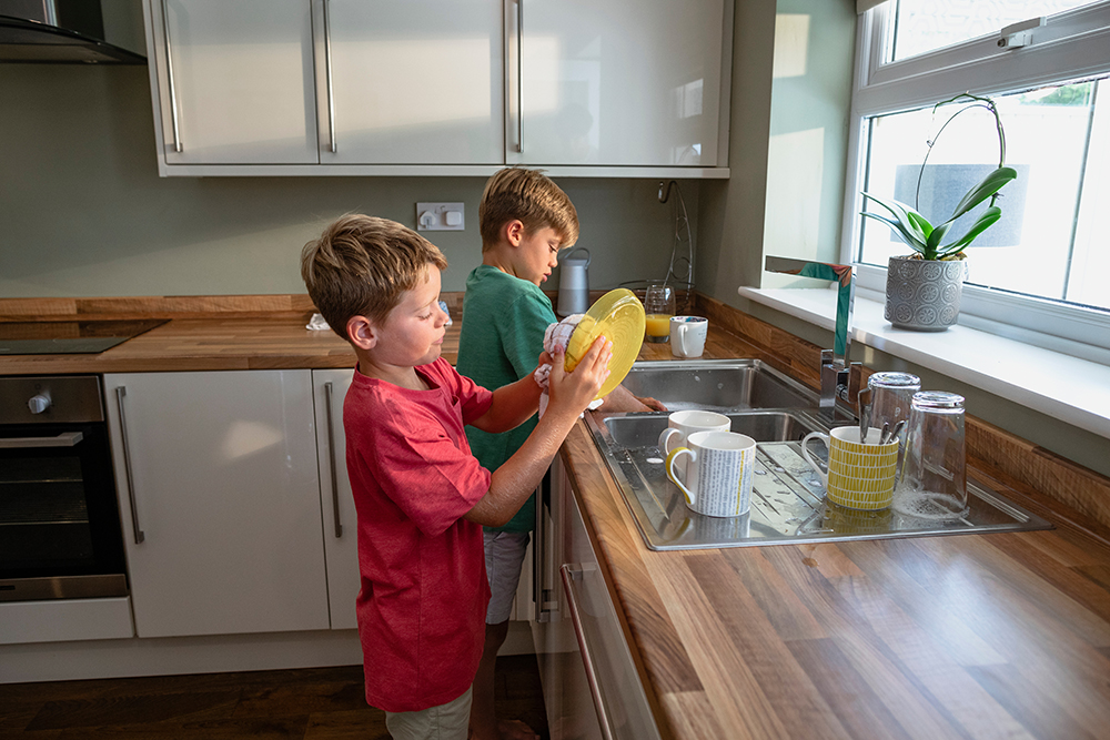 A side-view shot of two young brothers washing the dishes together.